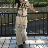 Person wearing a white t-shirt and beige pants with text, standing on a tiled floor.